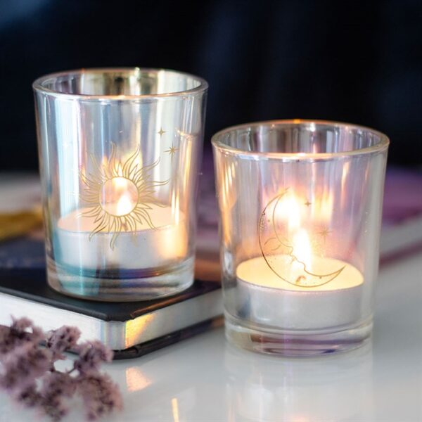 Two decorative candle holders with sun and moon designs, glowing softly on a surface.