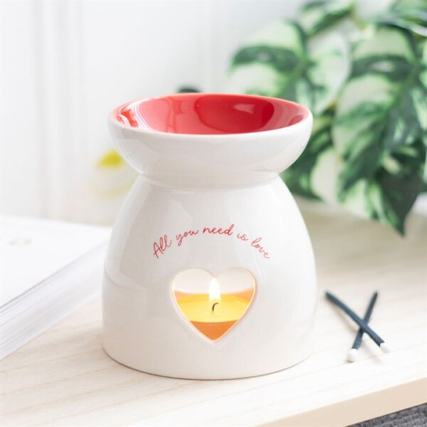 A decorative ceramic oil burner with a heart-shaped cutout and the phrase "All you need is love."