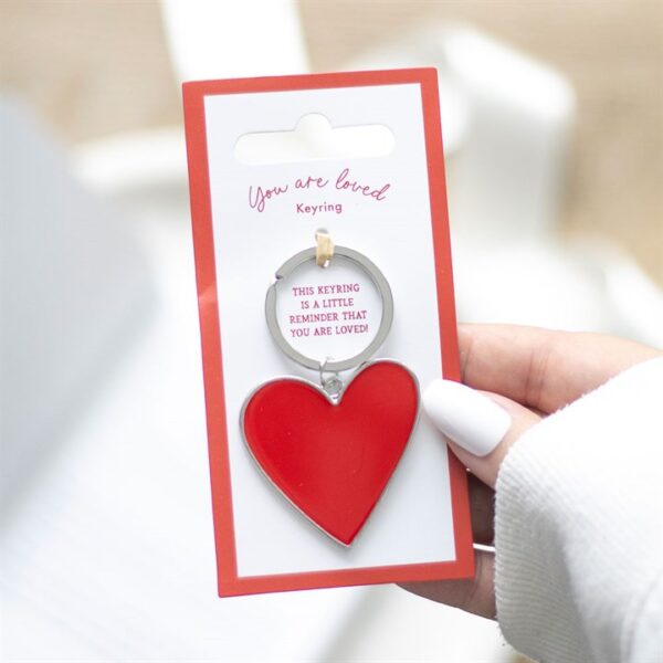 A hand holding a heart-shaped keyring with a tag saying "You are loved."