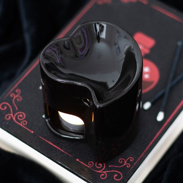 A black heart-shaped oil burner sits atop a patterned book with chopsticks beside it.