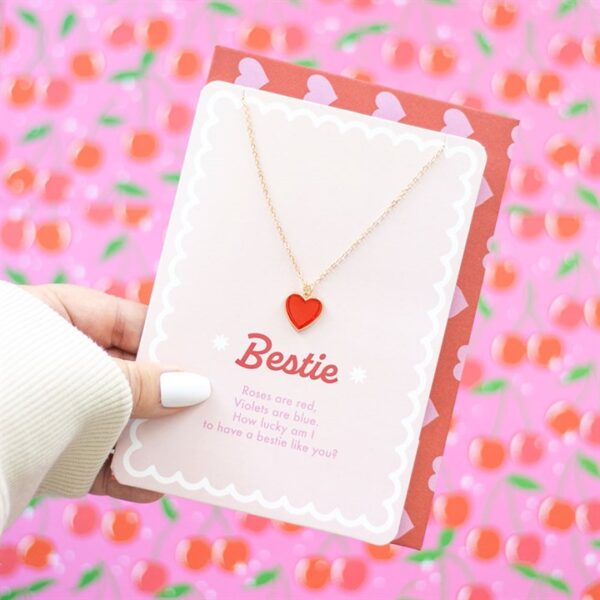 A hand holding a card with a heart necklace, celebrating friendship with a cheerful design.