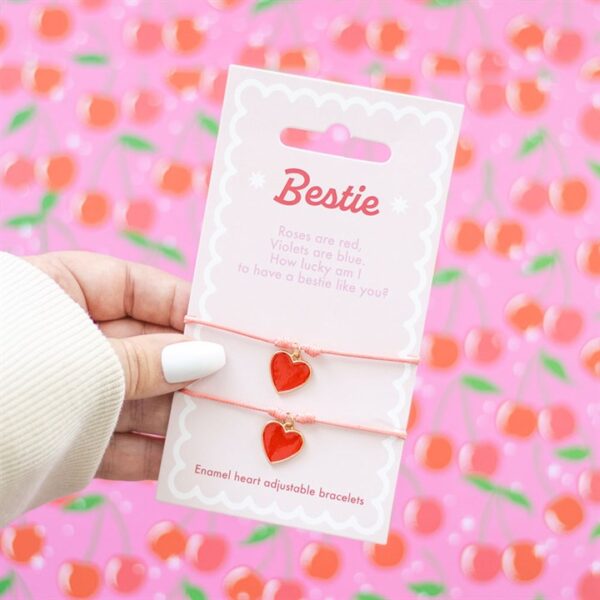 A hand holds a card with two red heart bracelets, labeled "Bestie" and decorated with poetry.