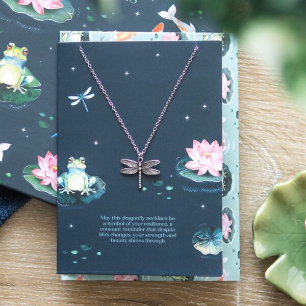 A dragonfly necklace displayed on a floral card, symbolizing resilience and inner strength.