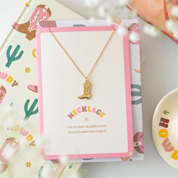 A gold cowboy boot necklace on a decorative card, surrounded by colorful themed items.