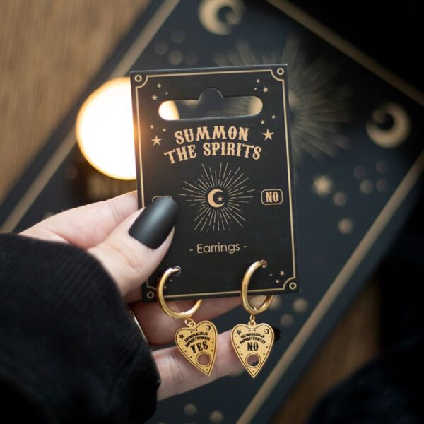 A hand holding a black earring card featuring "Summon the Spirits" with heart-shaped earrings.